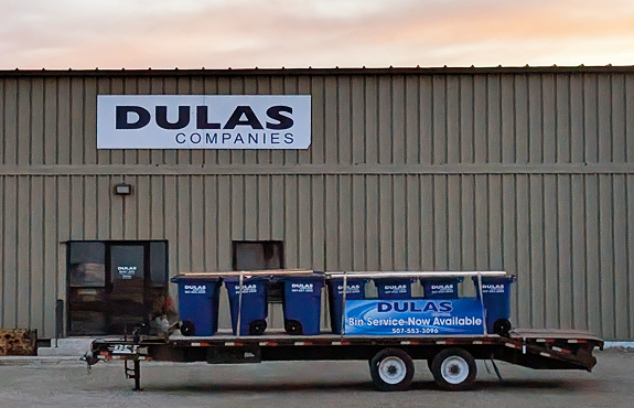 Dulas residential trash bins, on a trailer, in front of the entrance to Dulas Companies building.